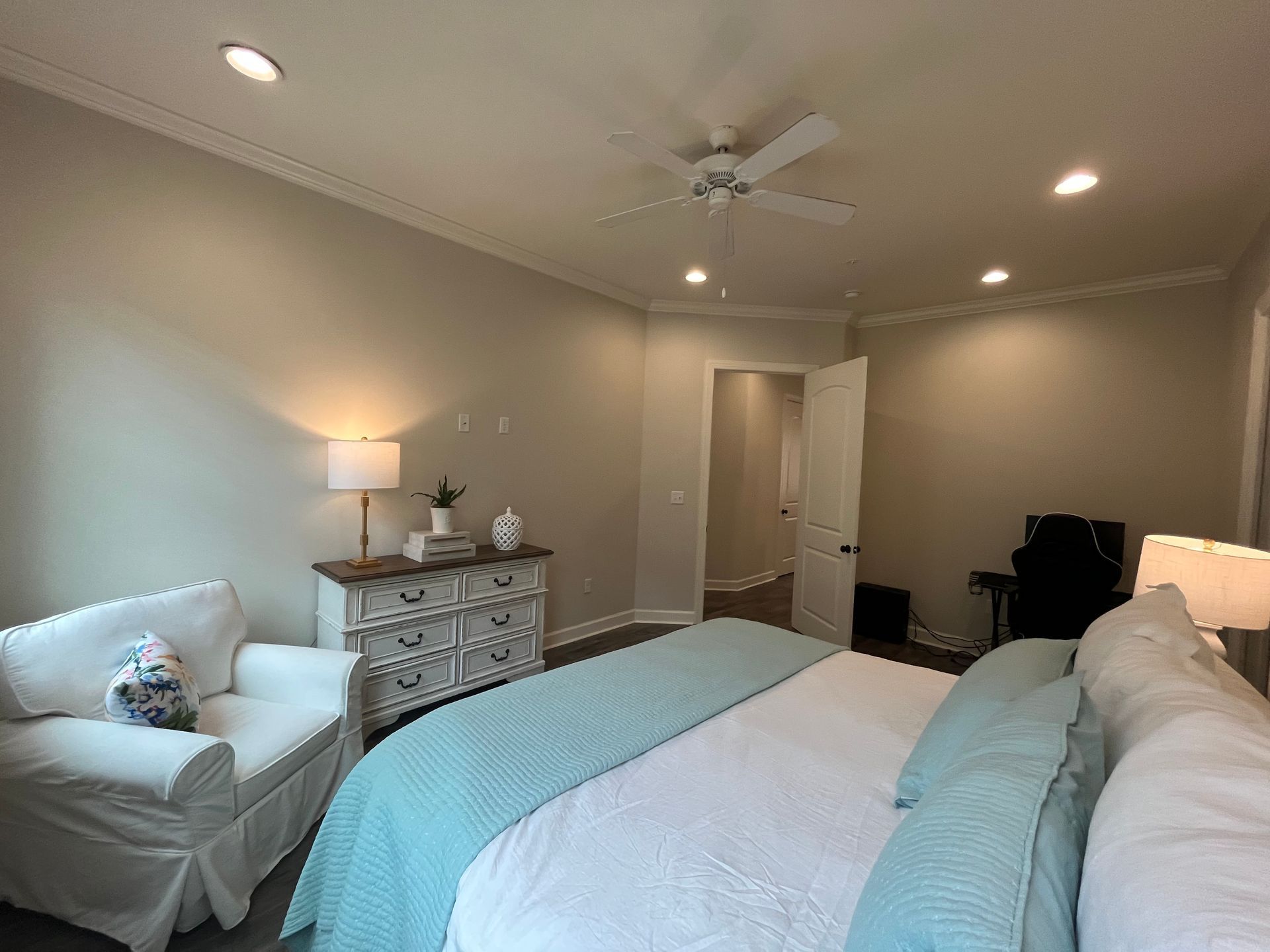 Bedroom with white bed, chair, dresser, and recessed lighting. Pale blue and white color scheme.