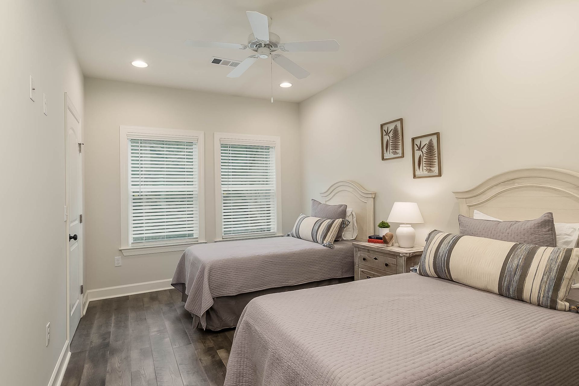 Bedroom with two twin beds, gray bedding, white headboards, windows, and a ceiling fan.