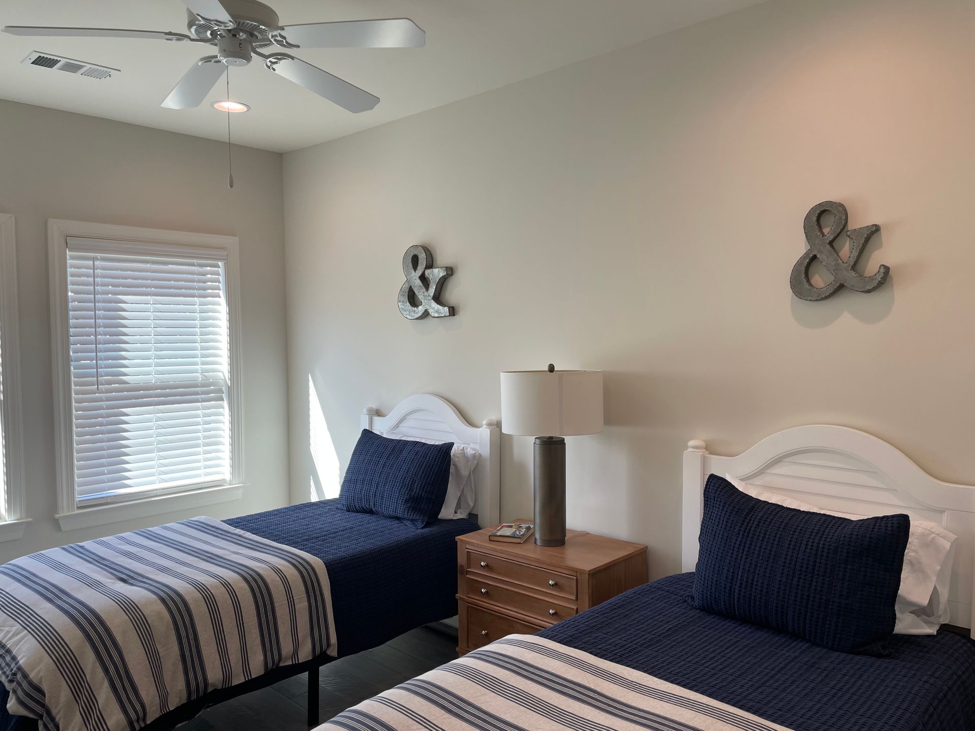 Two twin beds in a room with white walls, blue bedding, and a nightstand with a lamp.