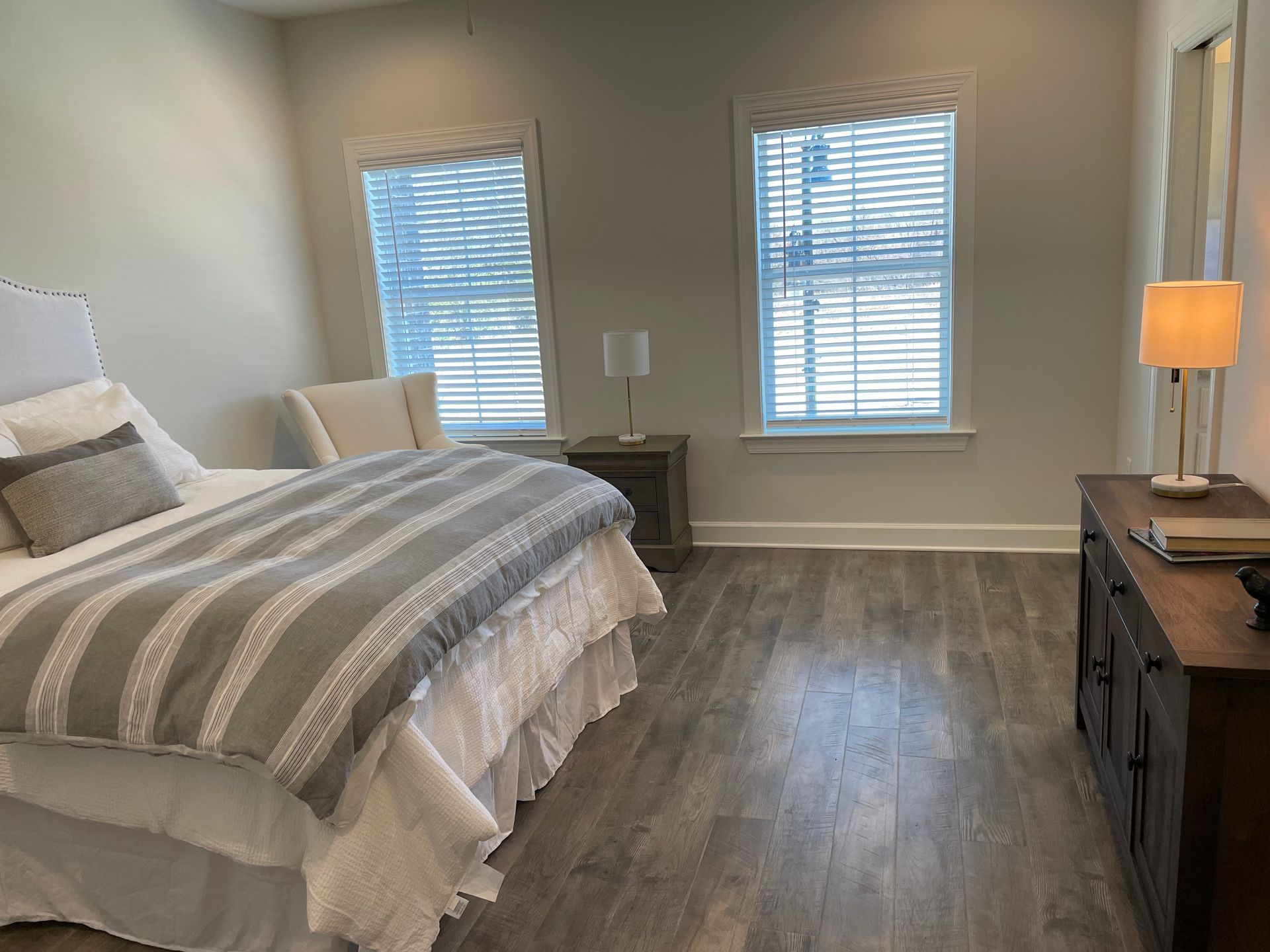 Bedroom with bed, nightstand, dresser, two windows, and wood flooring.