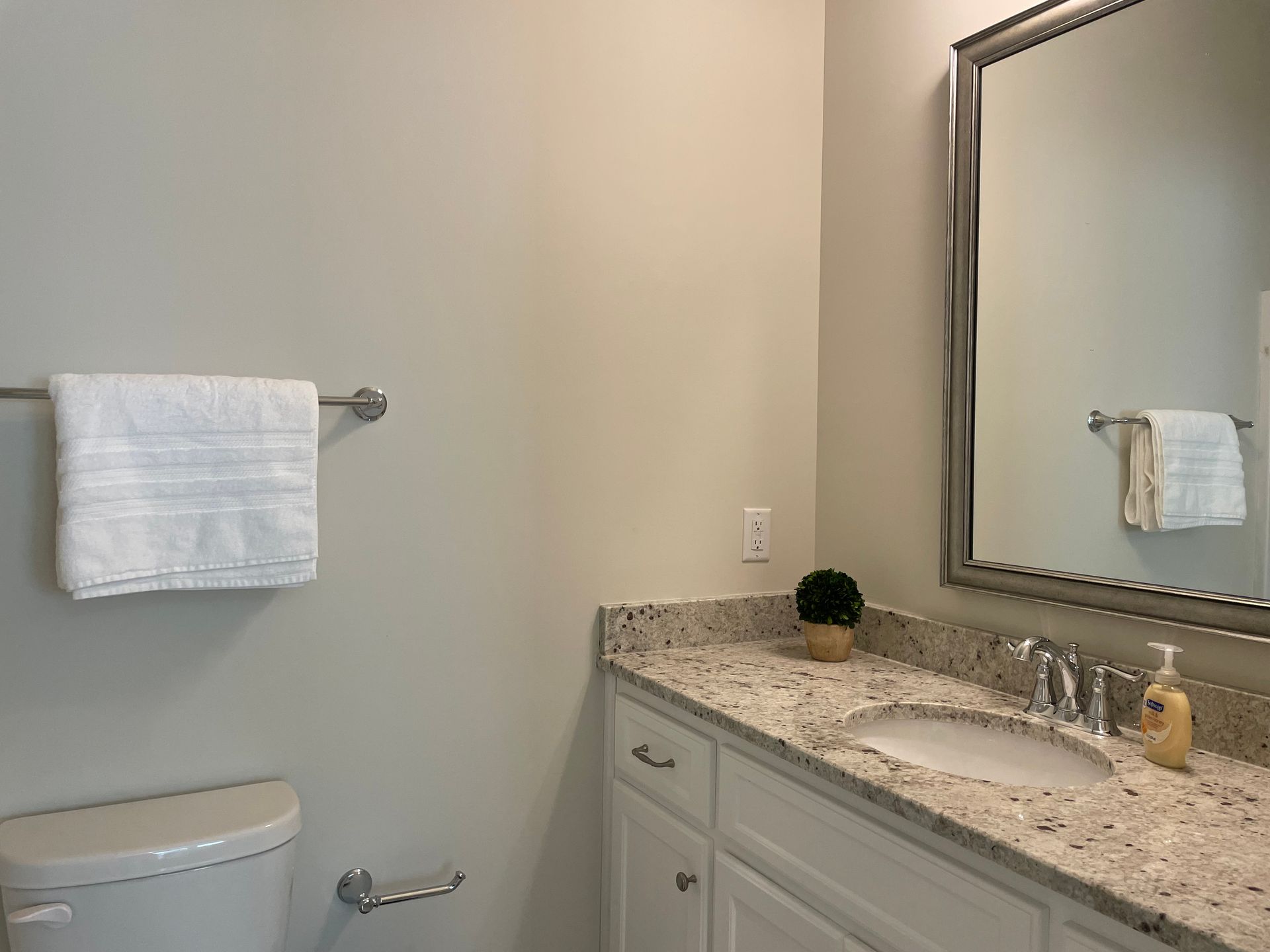 A small bathroom with a toilet, sink, mirror, and towel rack. Walls are light-colored.