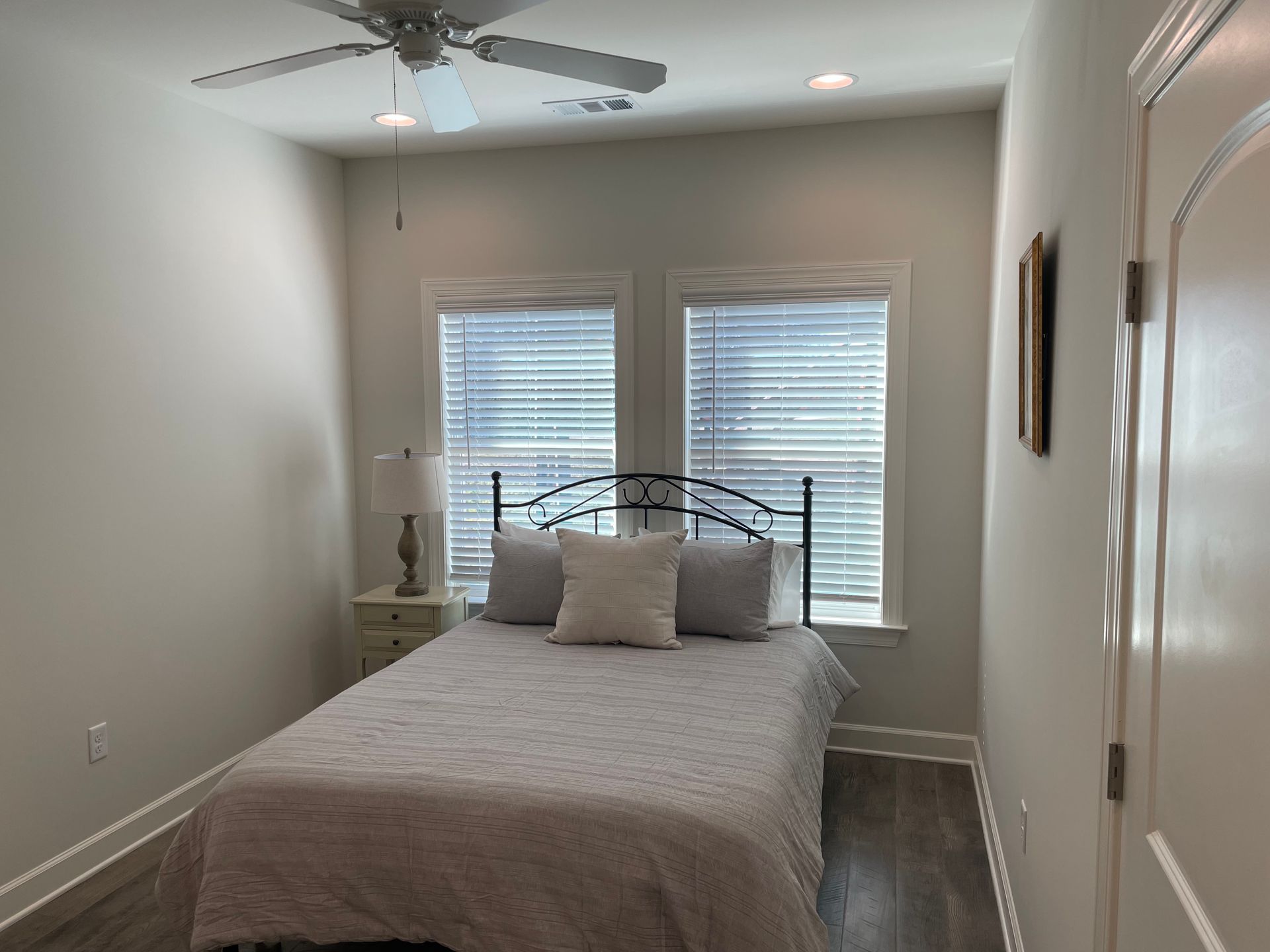 Small bedroom with bed, bedside table, two windows with blinds, and ceiling fan.