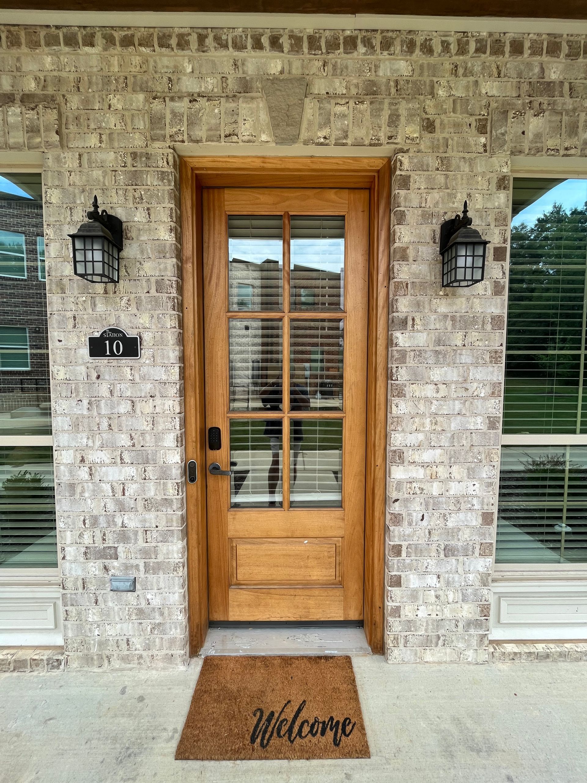 Wooden front door with glass panels and sidelights on a brick facade with sconces. 