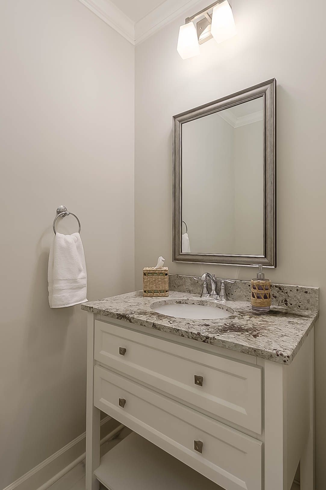Small bathroom with white vanity, granite countertop, silver-framed mirror, and towel ring.