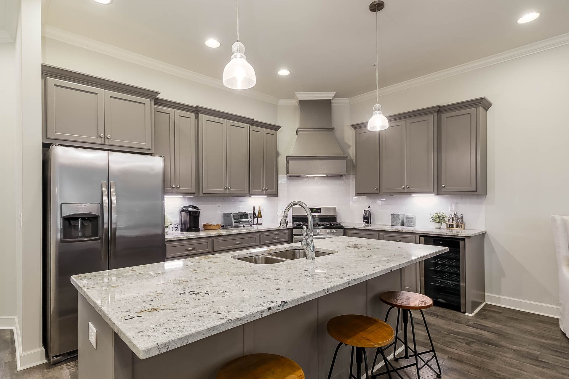 Modern kitchen with gray cabinets, stainless steel appliances, and a white granite island.