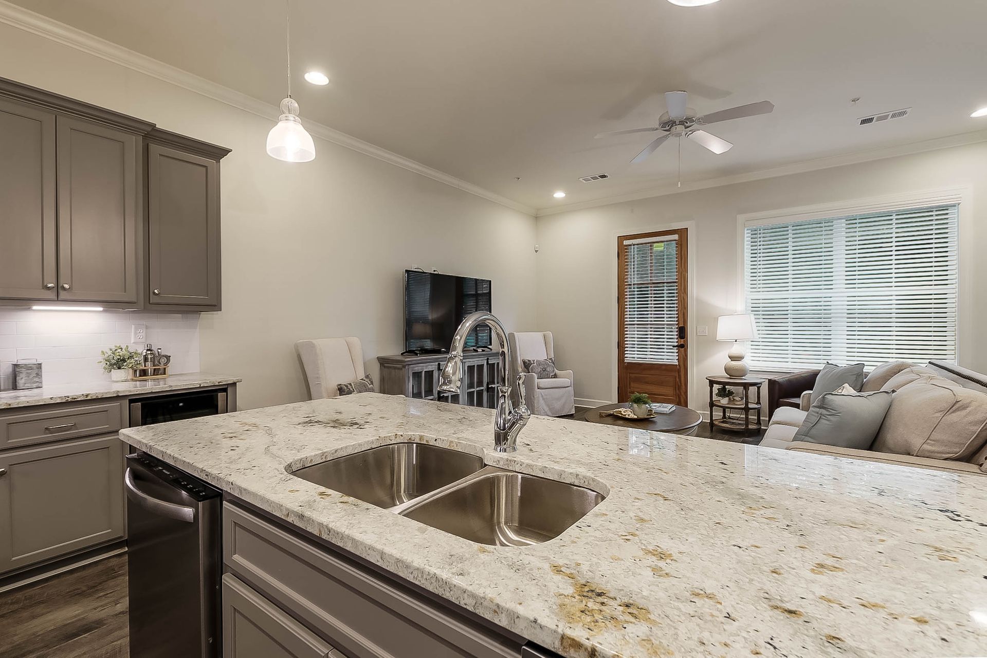 Kitchen with island, cabinets, and appliances; opens to living room with TV, sofa, and a door to the outside.