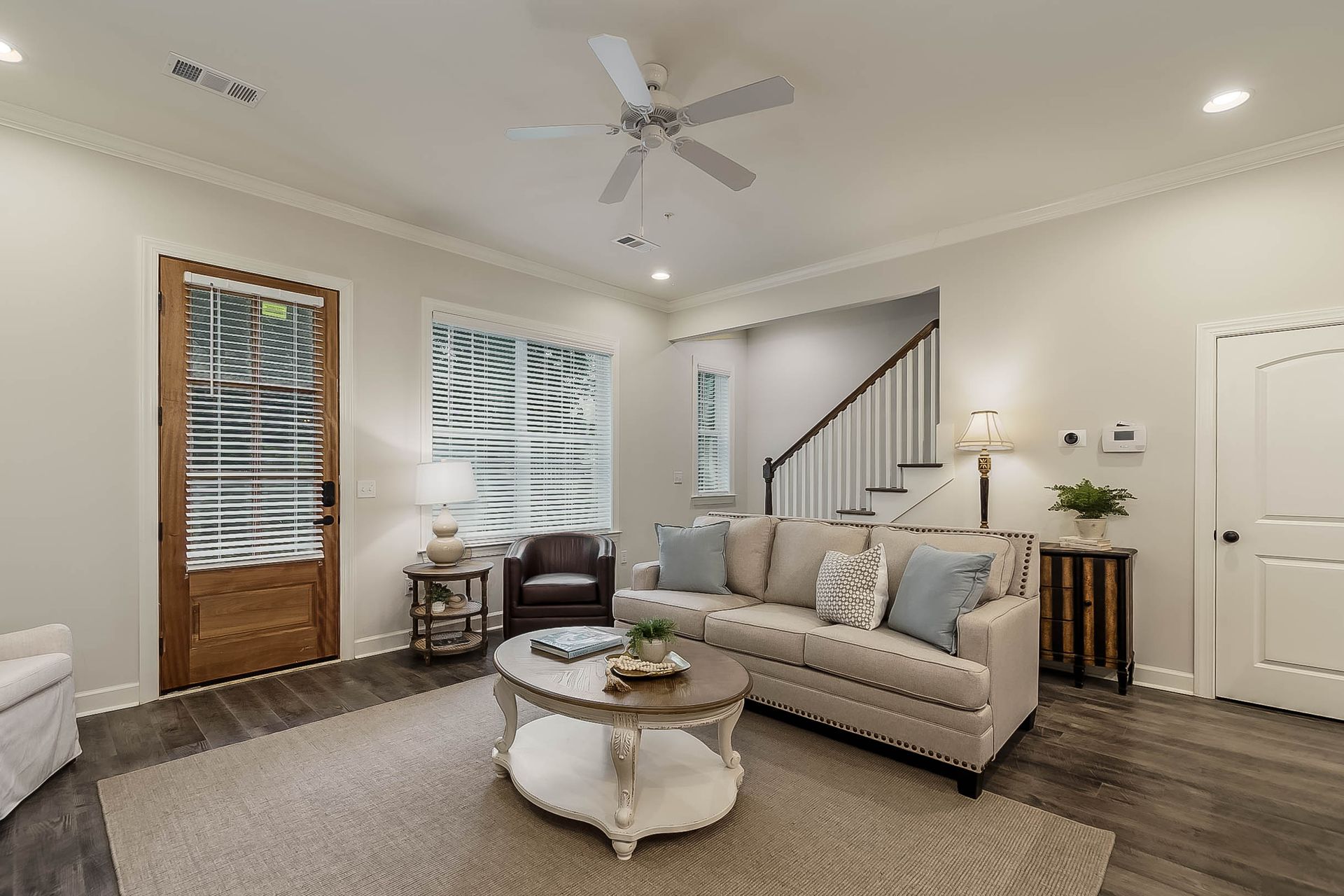 Living room with a sofa, coffee table, and stairs, wood floors, and white walls.