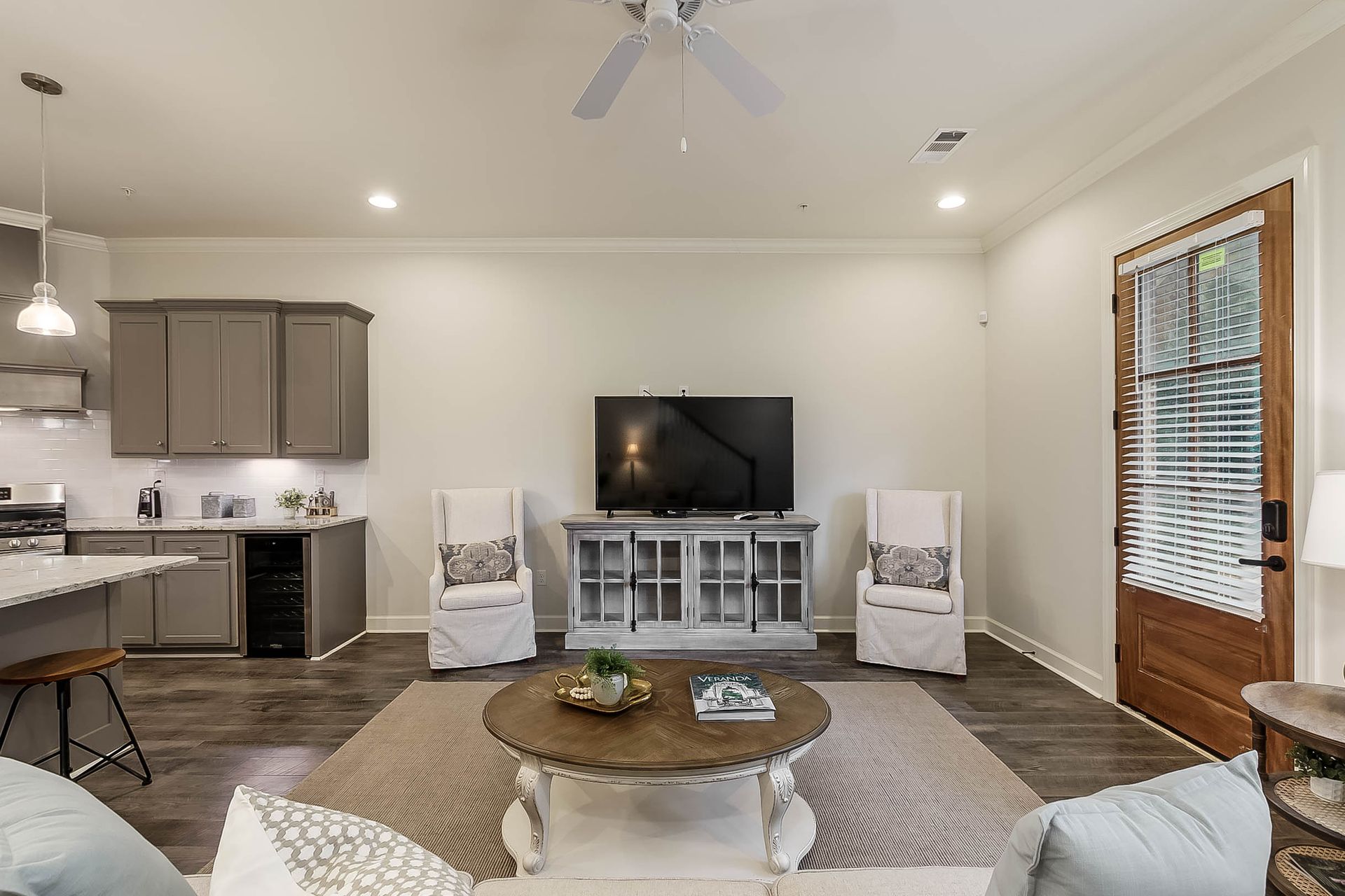 Living room with gray cabinets, TV, two white chairs, wooden door, and rug.