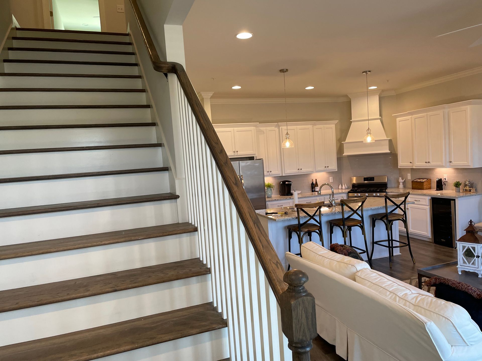Staircase leading up with dark wood treads and white risers; kitchen with white cabinets visible in the background.