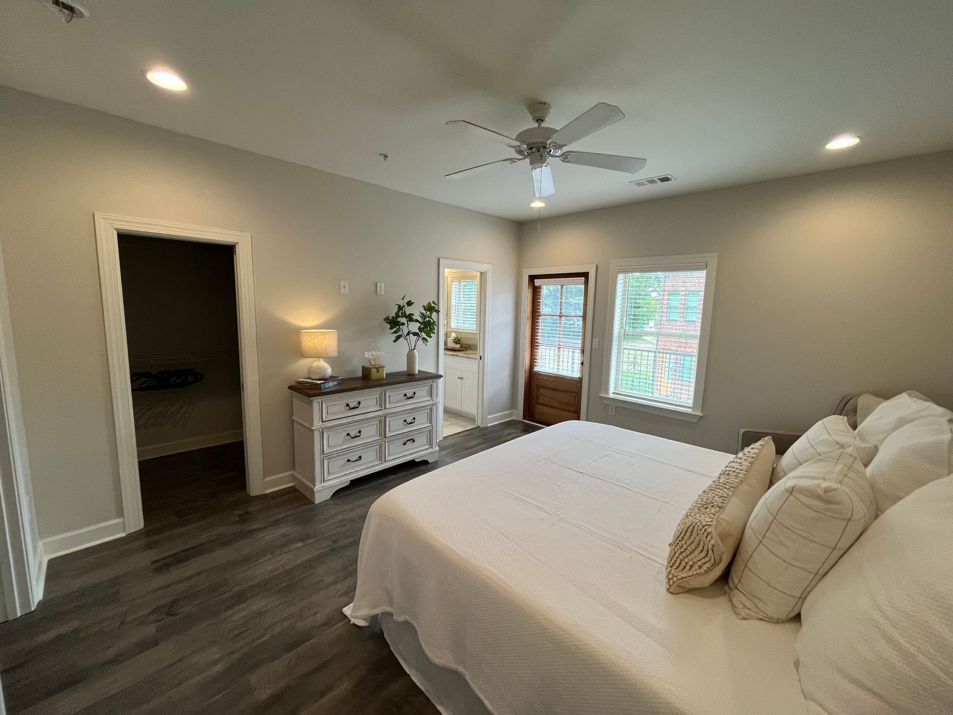Bedroom with a bed, dresser, doorway to bathroom and another room. Gray walls and flooring.