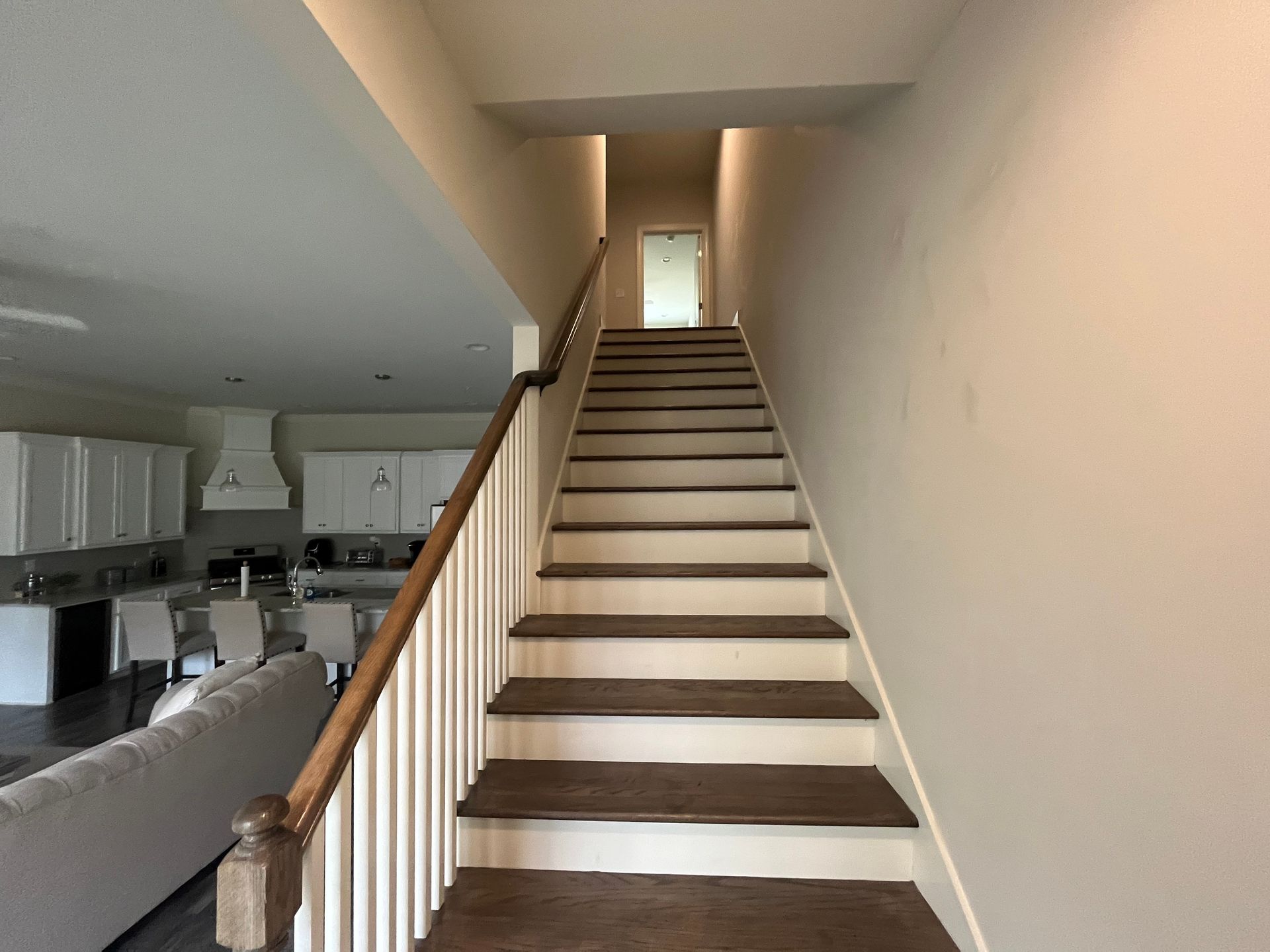 Staircase leads upwards; wood treads, white risers, railing on the left. The kitchen is visible on the left.