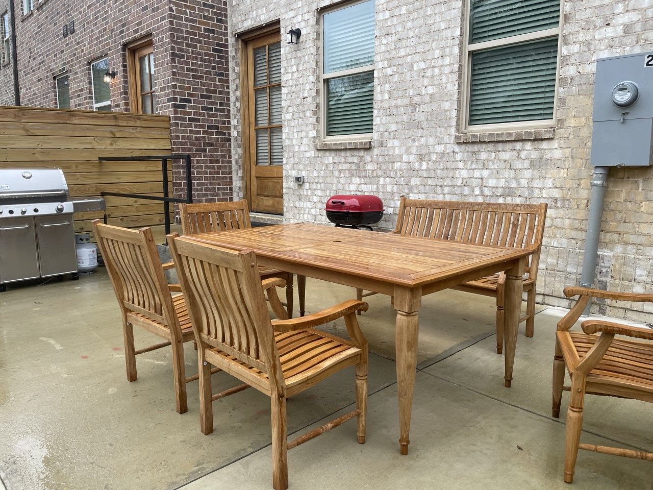 Patio with wooden table and chairs, brick wall, grill, and wooden privacy fence.