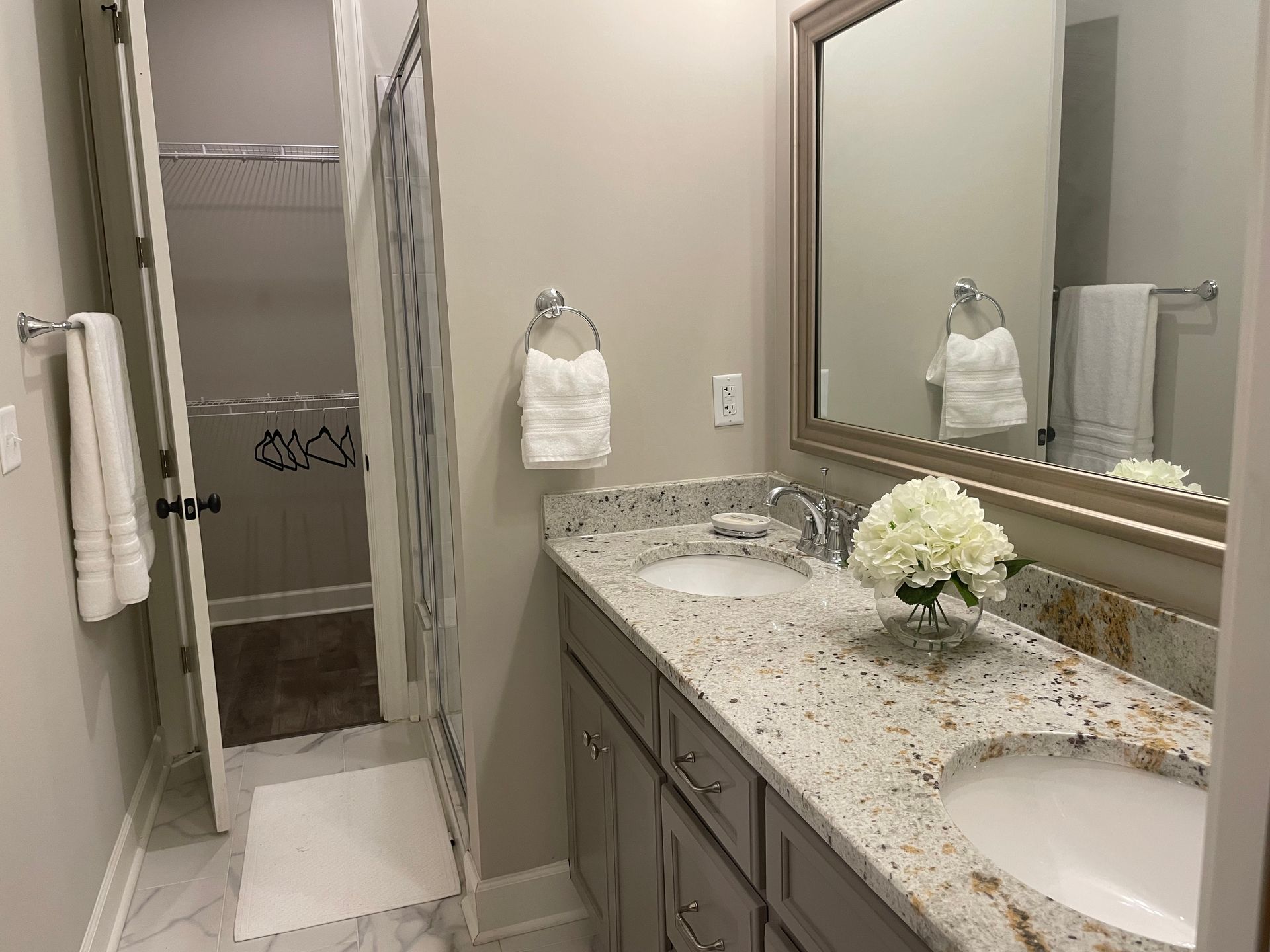 Bathroom with double sink, granite countertop, mirror, and open door to shower/closet. Gray and white tones.