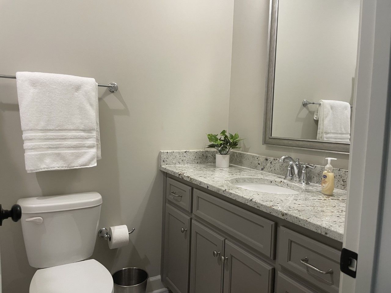 Bathroom with toilet, sink, mirror, towel rack, and light gray cabinets and walls.