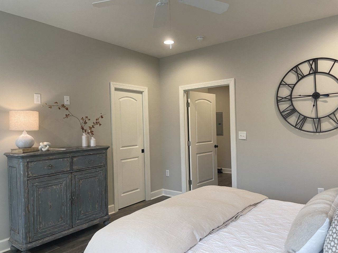 Bedroom with gray walls, antique cabinet, large clock, and bed. Two doors open into the room.