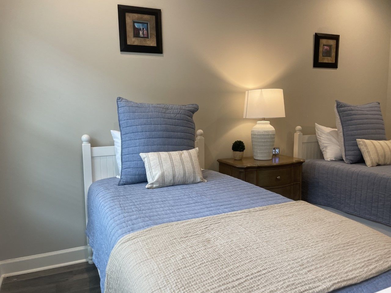 Two twin beds with blue and white bedding, a nightstand, and framed art.