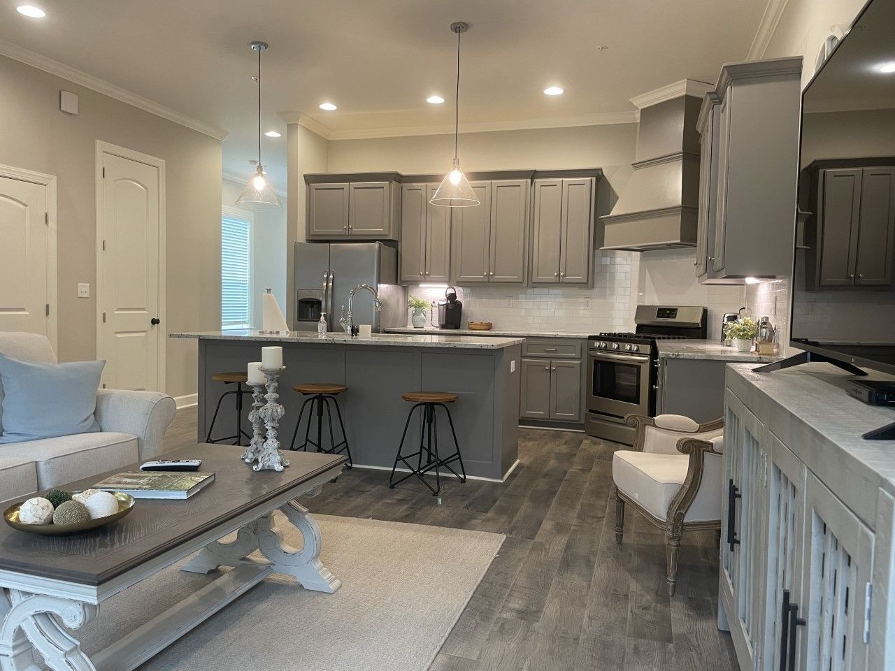 Open-concept kitchen and living area with gray cabinets, island, stainless steel appliances, and wood-look flooring.