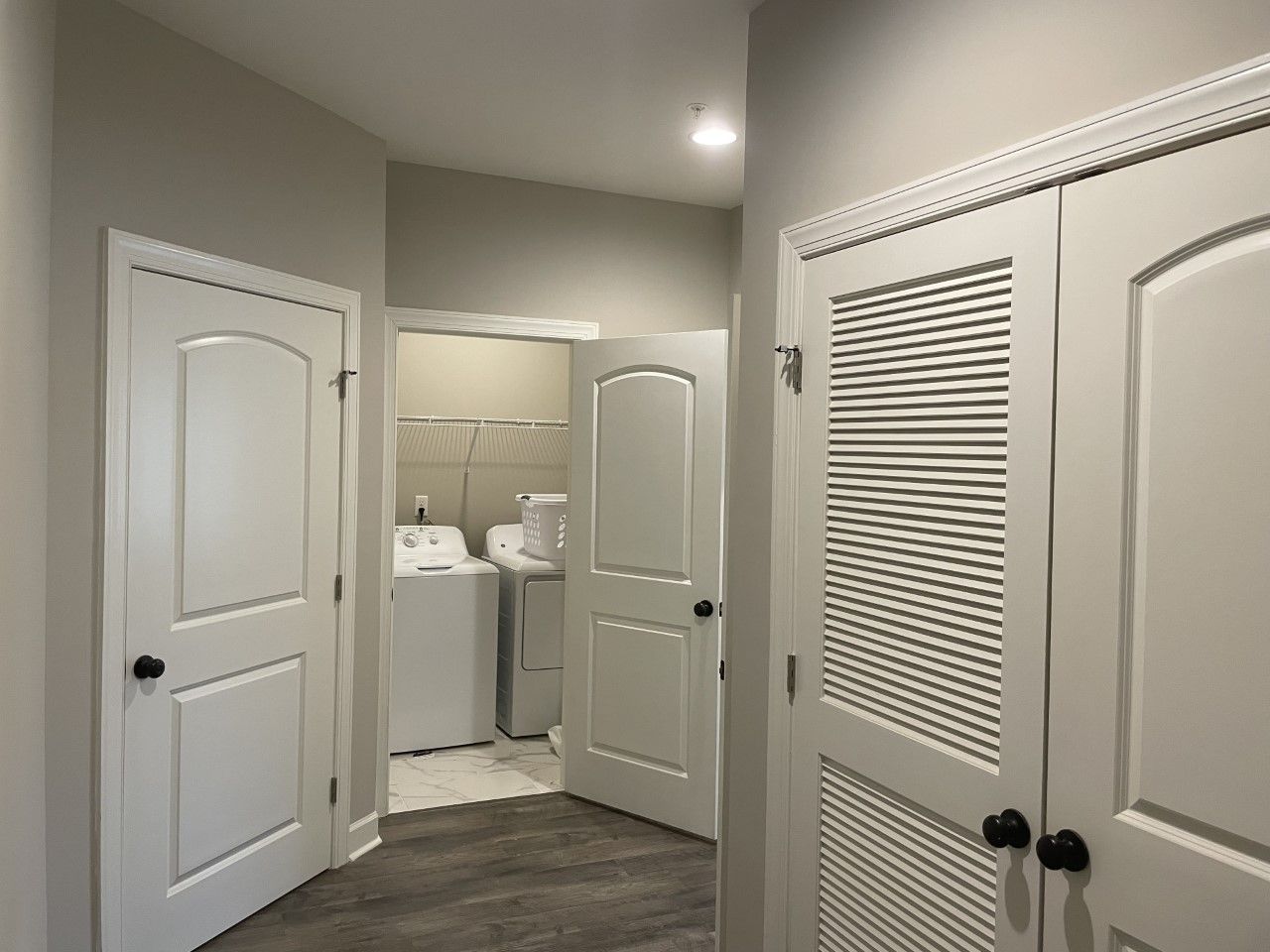 Hallway with white doors leading to laundry room, dark floor.