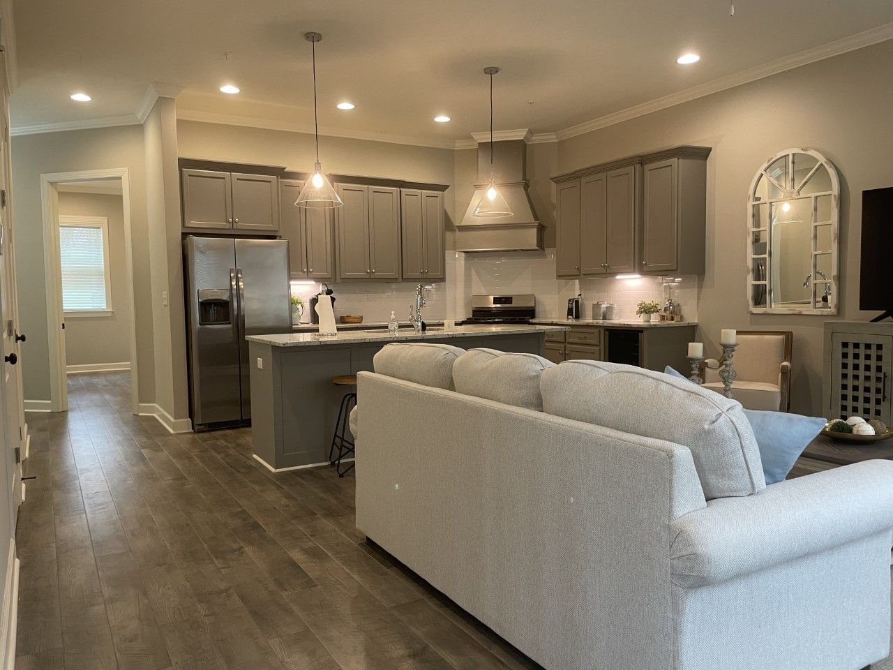 Open-concept kitchen and living room with gray cabinets, island, and sofa. Modern lighting and wood flooring.