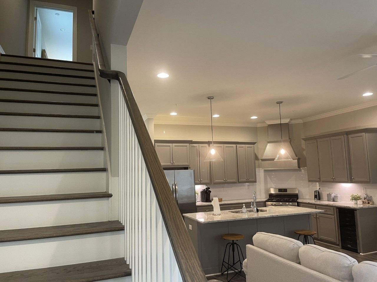 Interior view: staircase leading up; kitchen with gray cabinets, island, and seating.