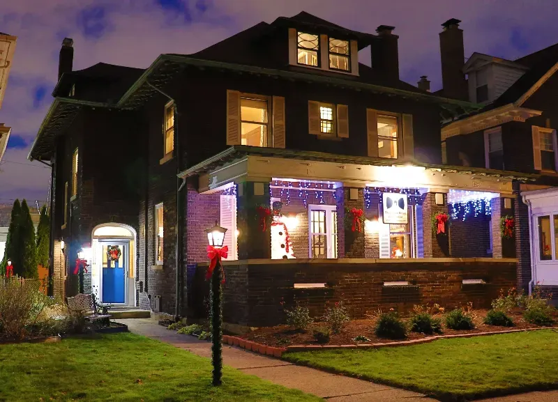 A large house with a porch decorated for christmas is lit up at night.