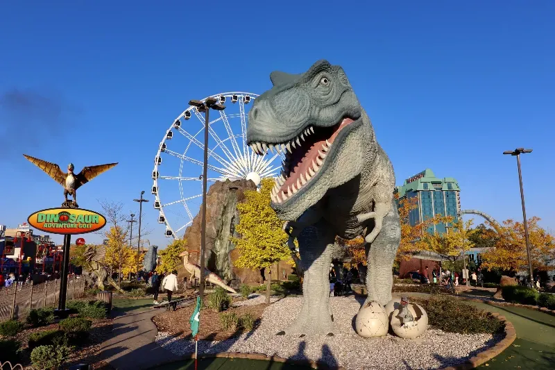 A statue of a dinosaur with a ferris wheel in the background.