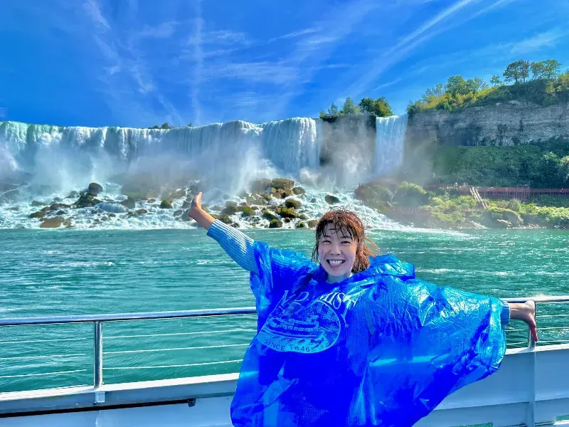 A woman in a blue poncho is standing on a boat in front of a waterfall.