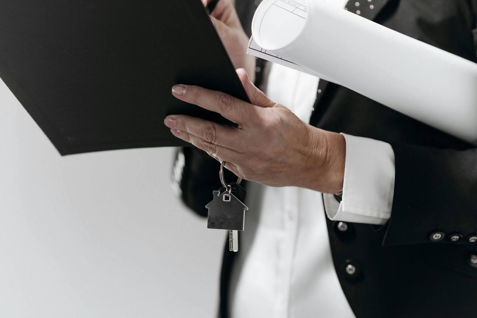 Real estate agent holding house keys and rolled-up blueprints