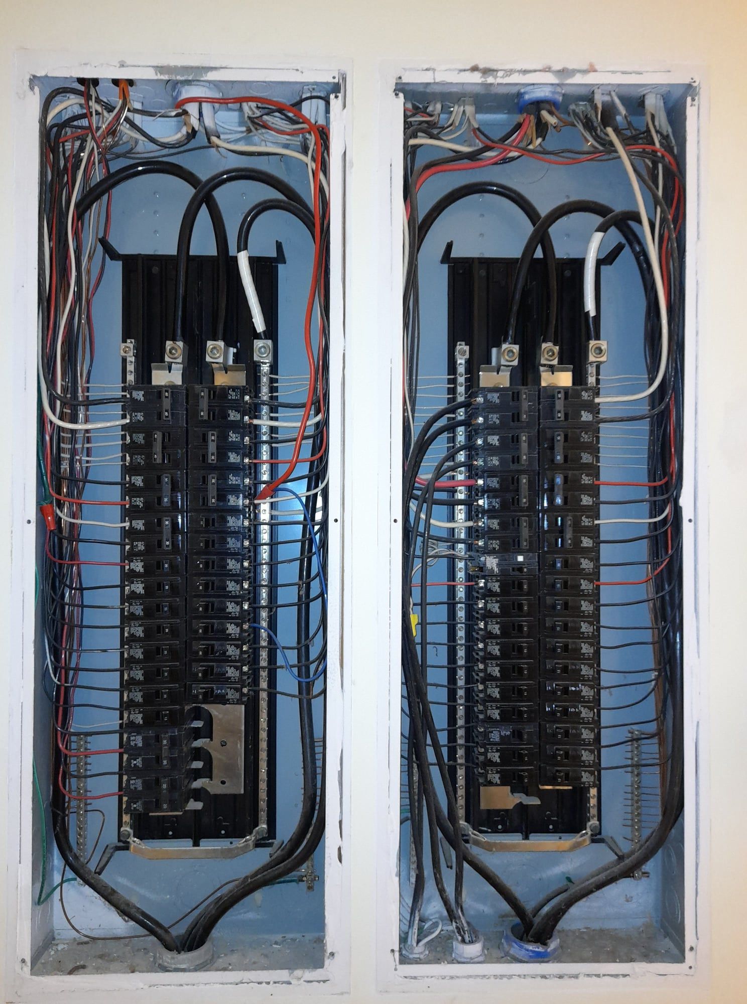 Two electrical breaker panels in a wall, wiring visible; black and colored wires.