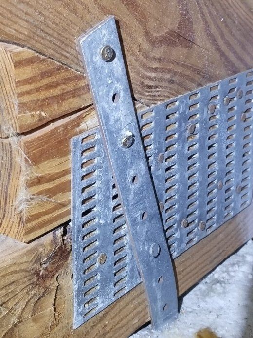 Two metal straps attached to wooden beams with screws. Perforated metal on one strap.