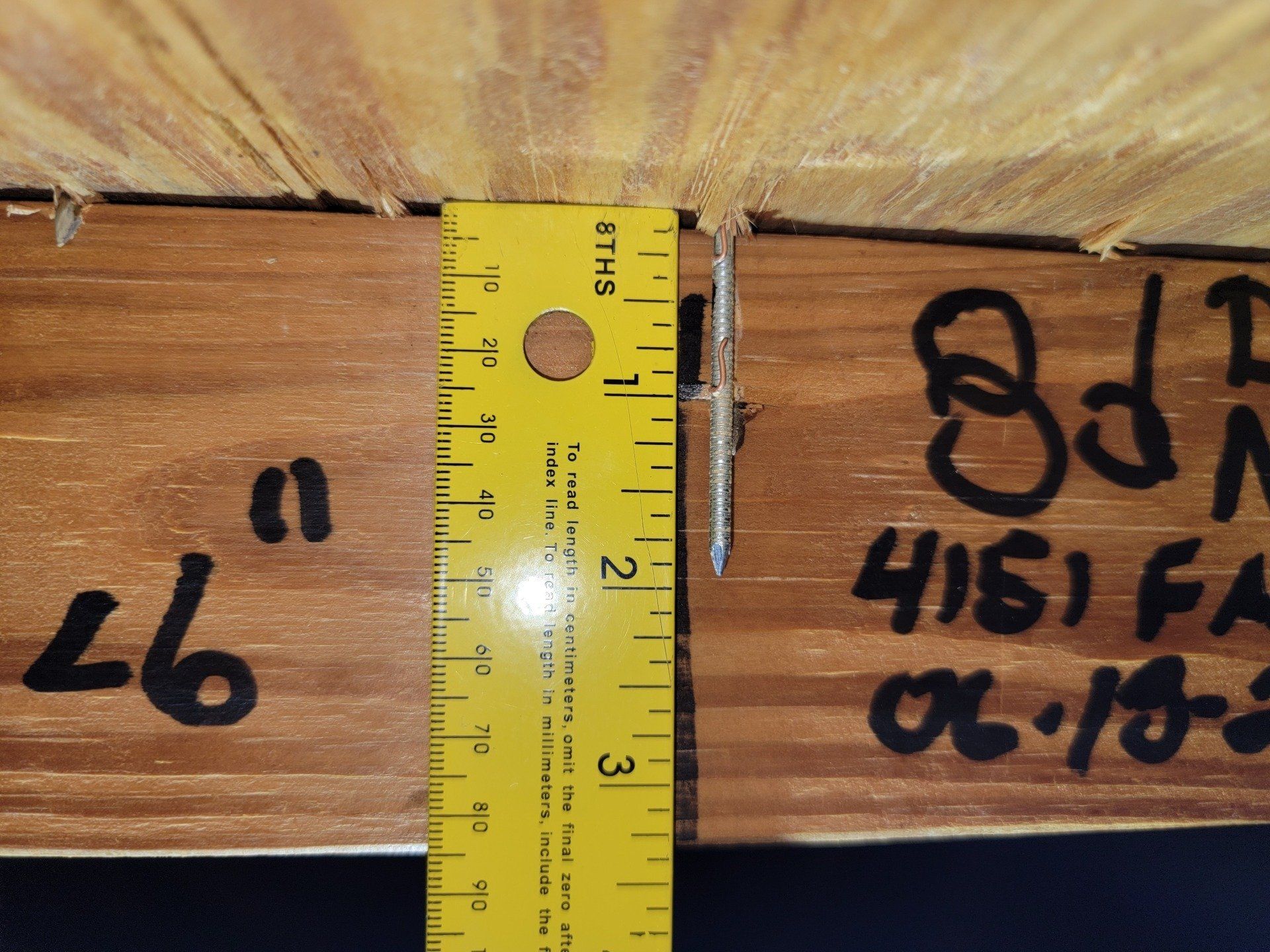 Yellow ruler measuring the distance between two pieces of wood. Handwritten text and nails are visible.
