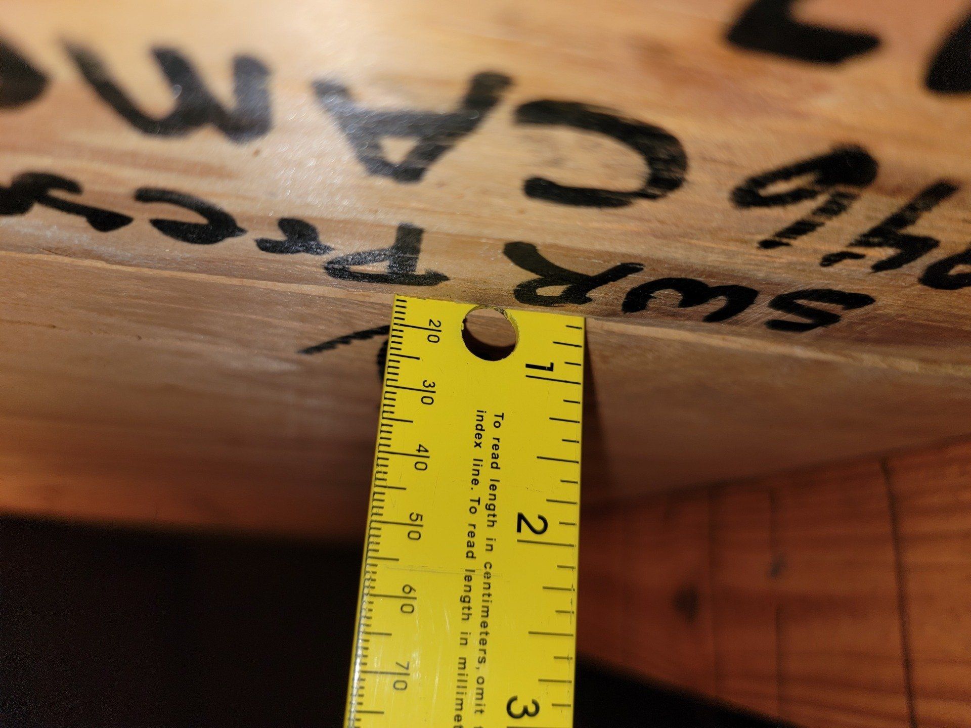 A yellow ruler measures the depth of a wooden surface, with markings showing the measurement is around 1/2 inch.