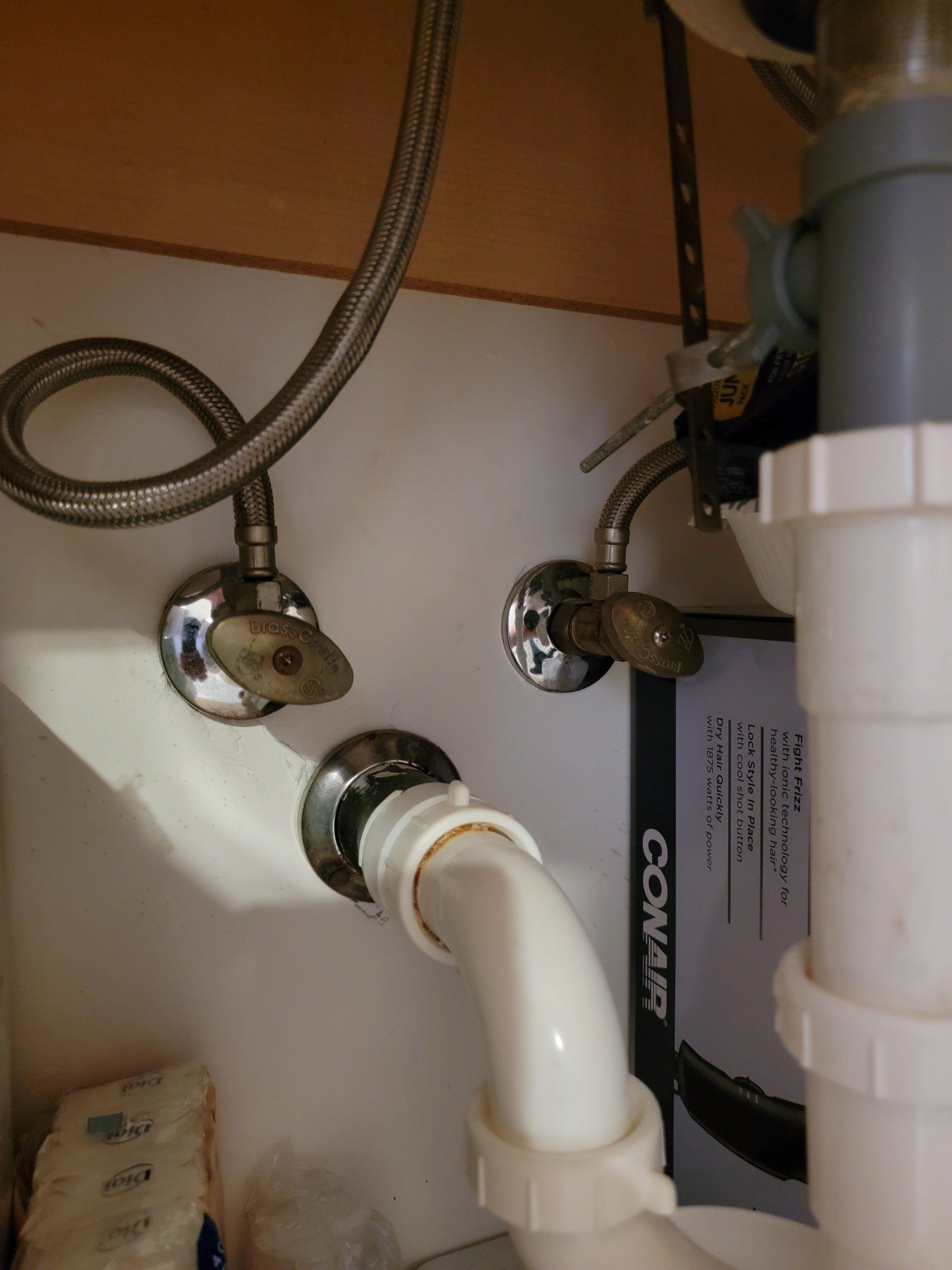 Plumbing under a bathroom sink: water supply valves, drainpipe, and a flexible supply line.