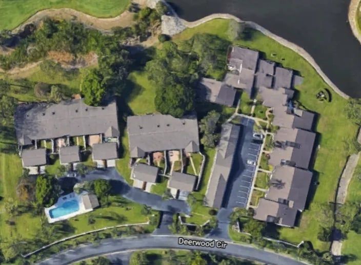 Aerial view of townhouses with gray roofs, a pool, and green landscaping. Located on Deerwood Ct.
