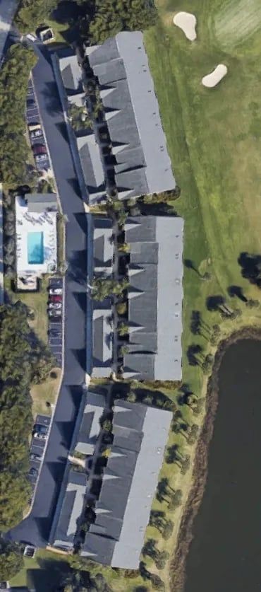 Aerial view of townhouses with gray roofs, pool, and golf course. A lake borders the townhouses.