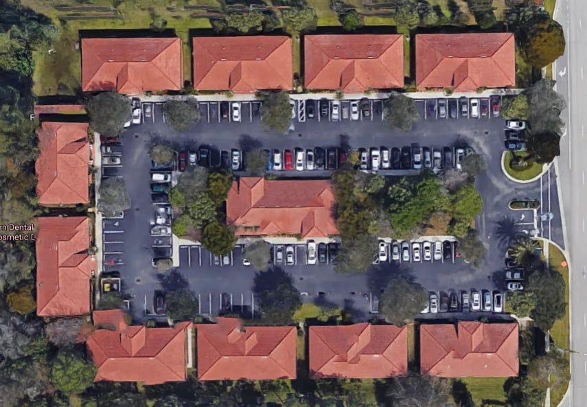 Aerial view of a complex with red tile roofs, multiple buildings, and parking lots with parked cars.