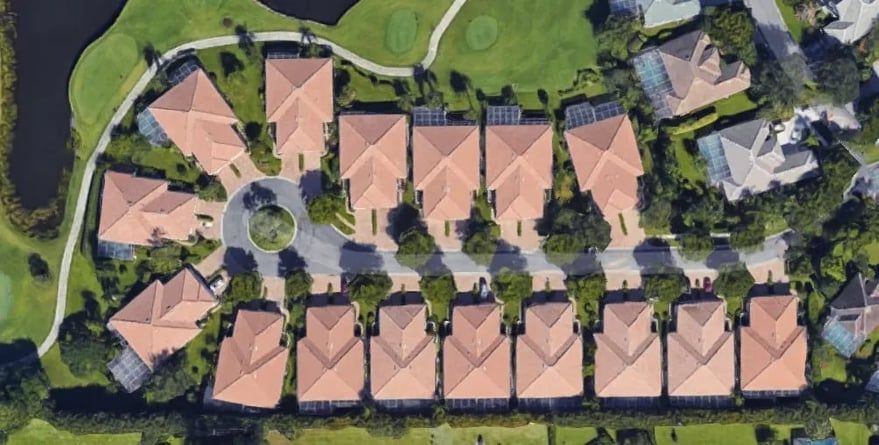 Aerial view of a suburban neighborhood with rows of houses, orange roofs, and a central circular road.