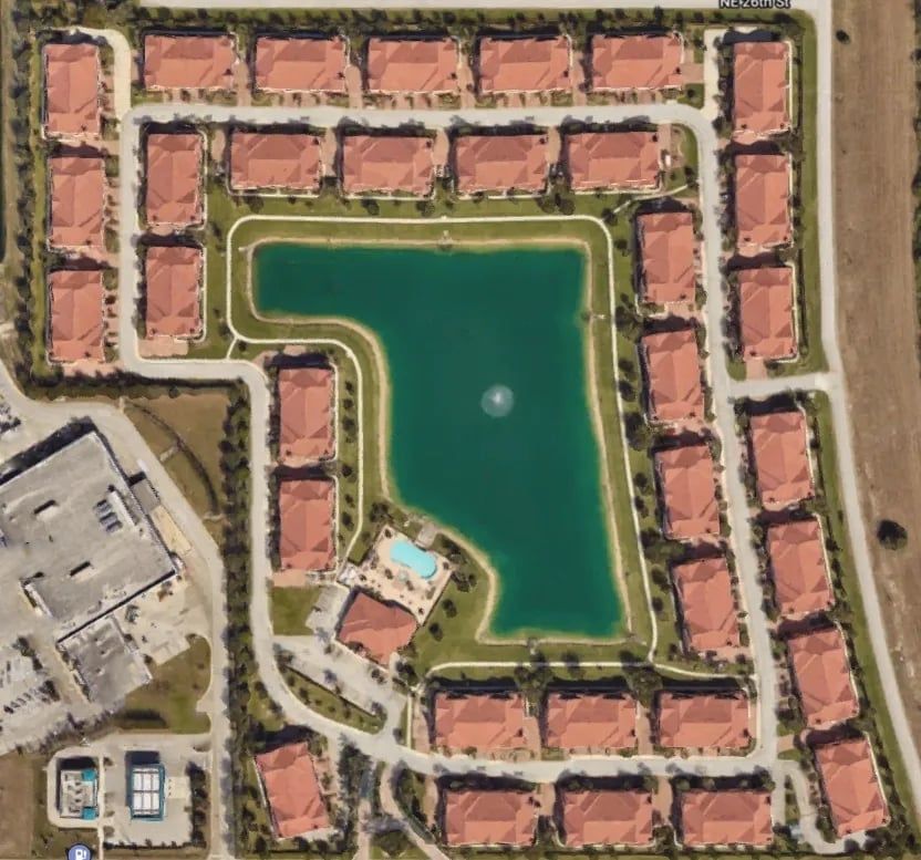 Aerial view of a residential community with a lake in the center, surrounded by buildings and streets.
