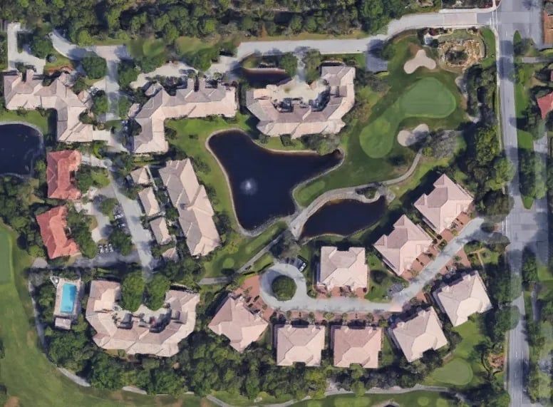 Aerial view of a residential complex with buildings, a pond, a small golf course, and trees.