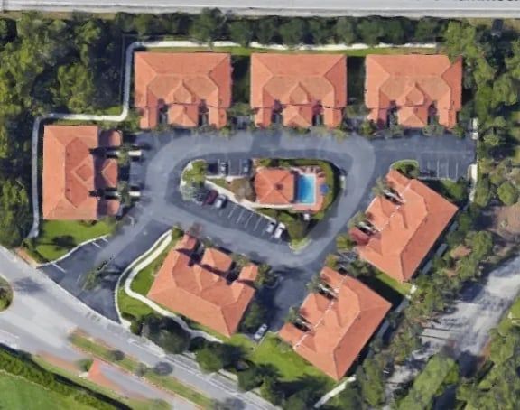 Aerial view of a complex with red-tiled roofs, a pool, parking, and greenery.