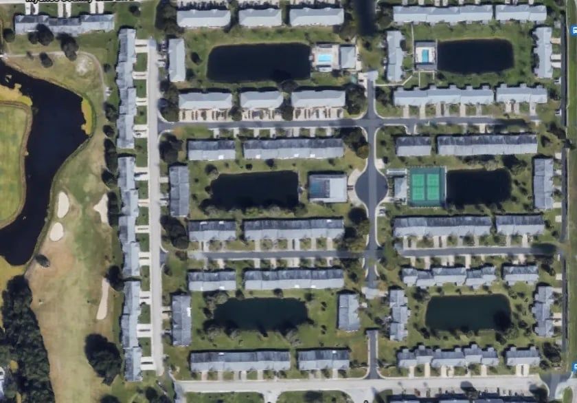 Aerial view of a residential community with townhouses, ponds, tennis courts, and a golf course.