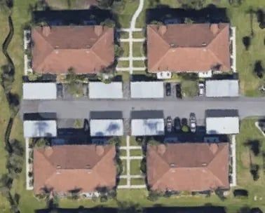 Aerial view of four apartment buildings with red tile roofs and parking shelters.