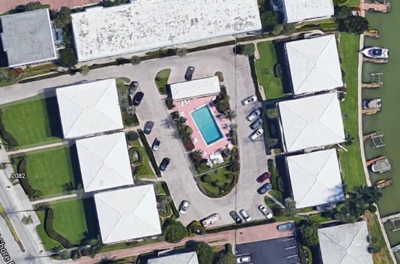 Aerial view of a complex with white buildings, a pool, parking, and a canal.