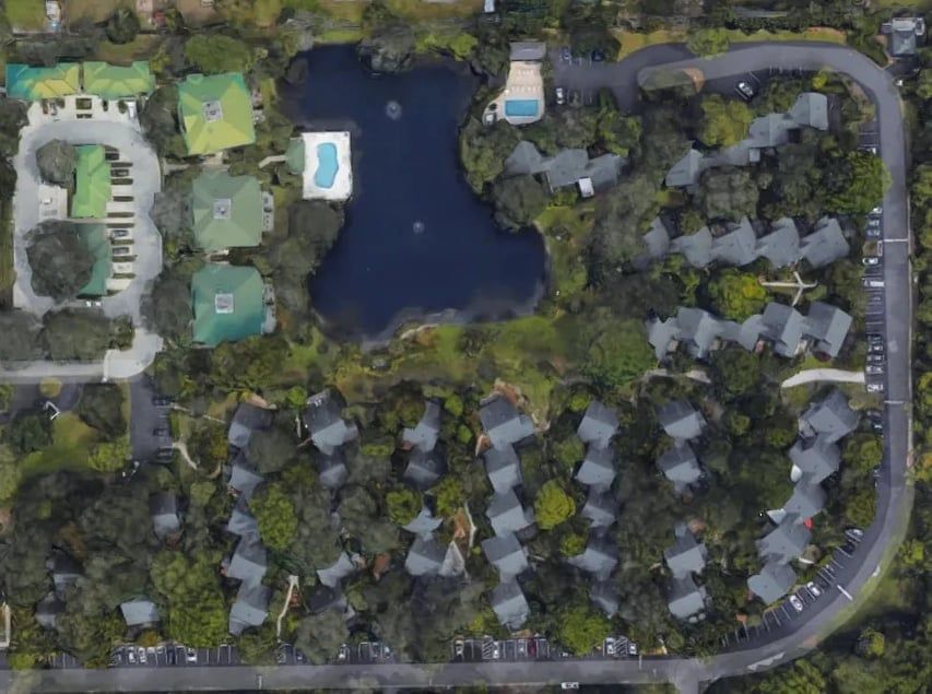 Aerial view of a resort with buildings, a lake, swimming pool, and trees.