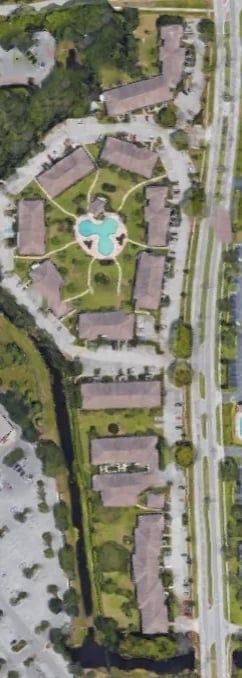 Aerial view of an apartment complex with a pool, buildings, trees, and roads.