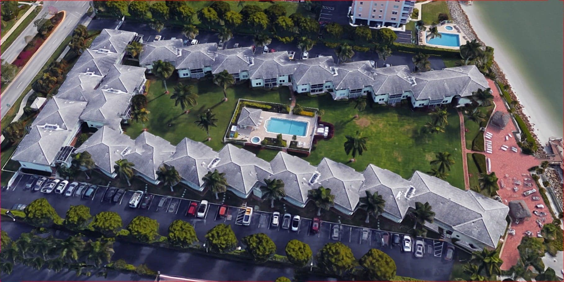 Aerial view of a complex with buildings, a pool, a green area, and a beach nearby.
