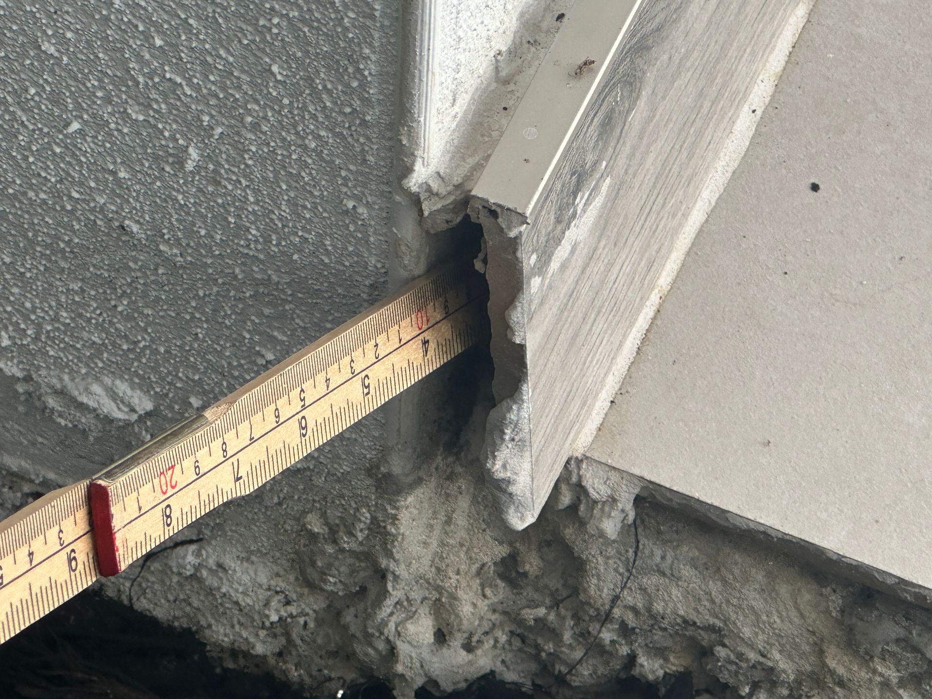 Close-up of a damaged corner where a ruler is used to measure an opening between materials of different textures and colors.