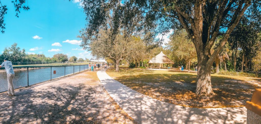 Park scene with trees, a paved path, water and a gazebo under a blue sky.