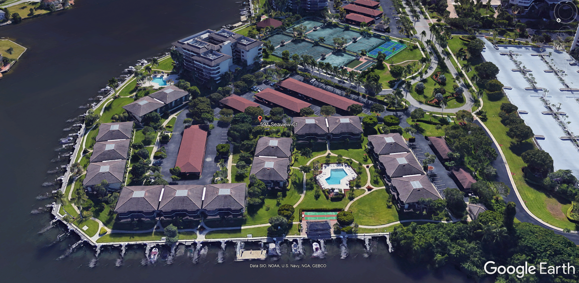 Aerial view of island with buildings, boats, pool, and green space, likely a waterfront residential community.