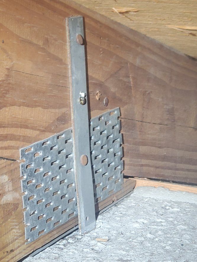 Metal bracket connecting wooden beams in an attic.